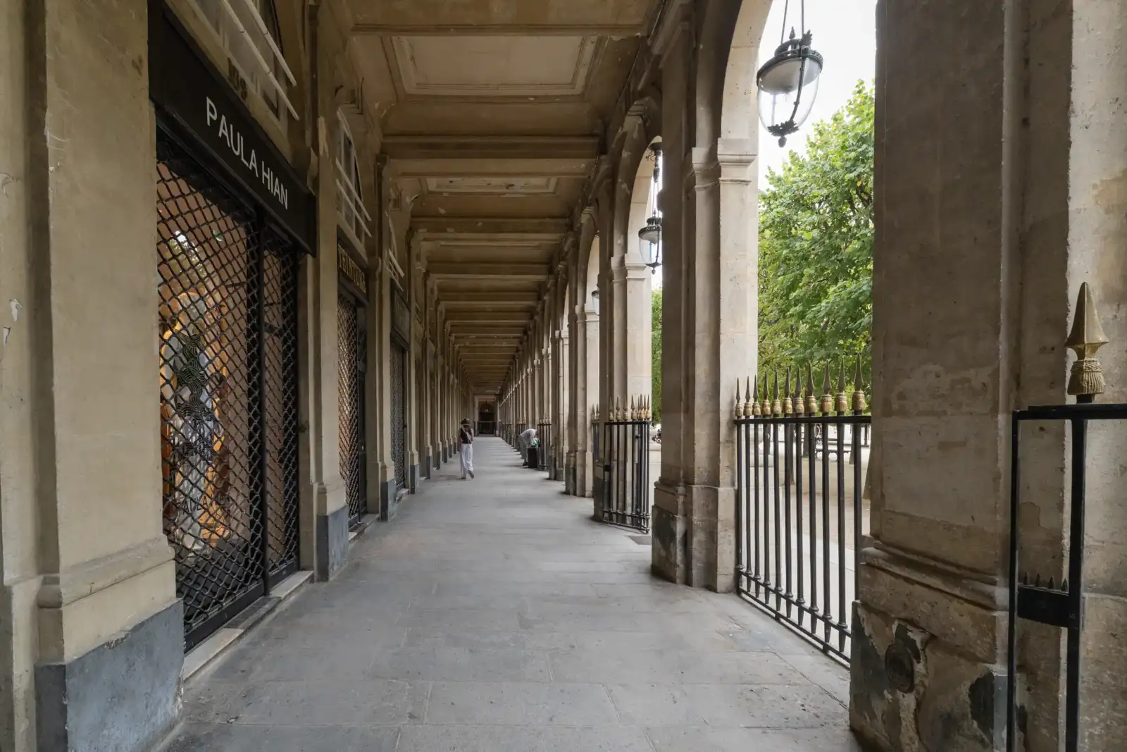 Vue en perspective d'une longue galerie couverte bordée de boutiques et de lourds piliers.