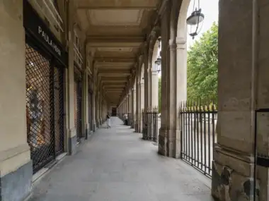 Vue en perspective d'une longue galerie couverte bordée de boutiques et de lourds piliers.