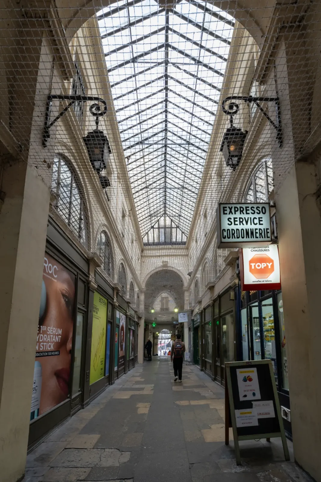 Une personne marche dans le Passage Vendôme à Paris sous une verrière historique lumineuse.