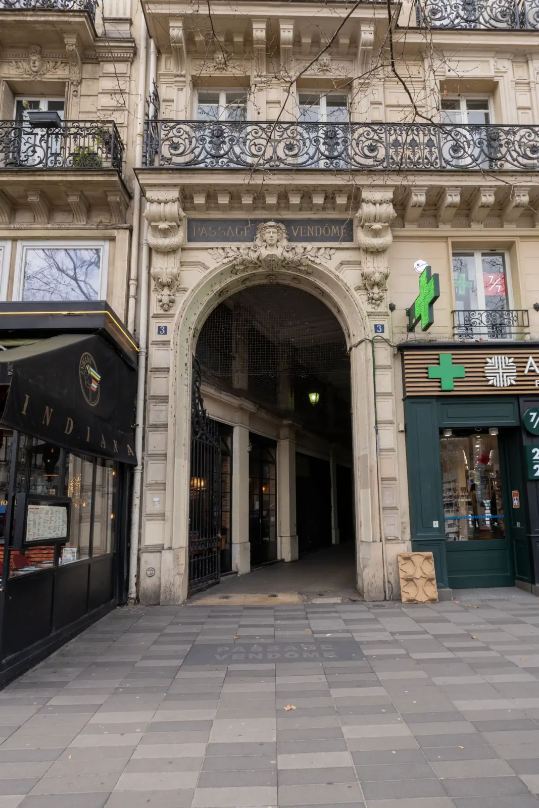 L'entrée en pierre sculptée du Passage Vendôme à Paris avec ses commerces adjacents.