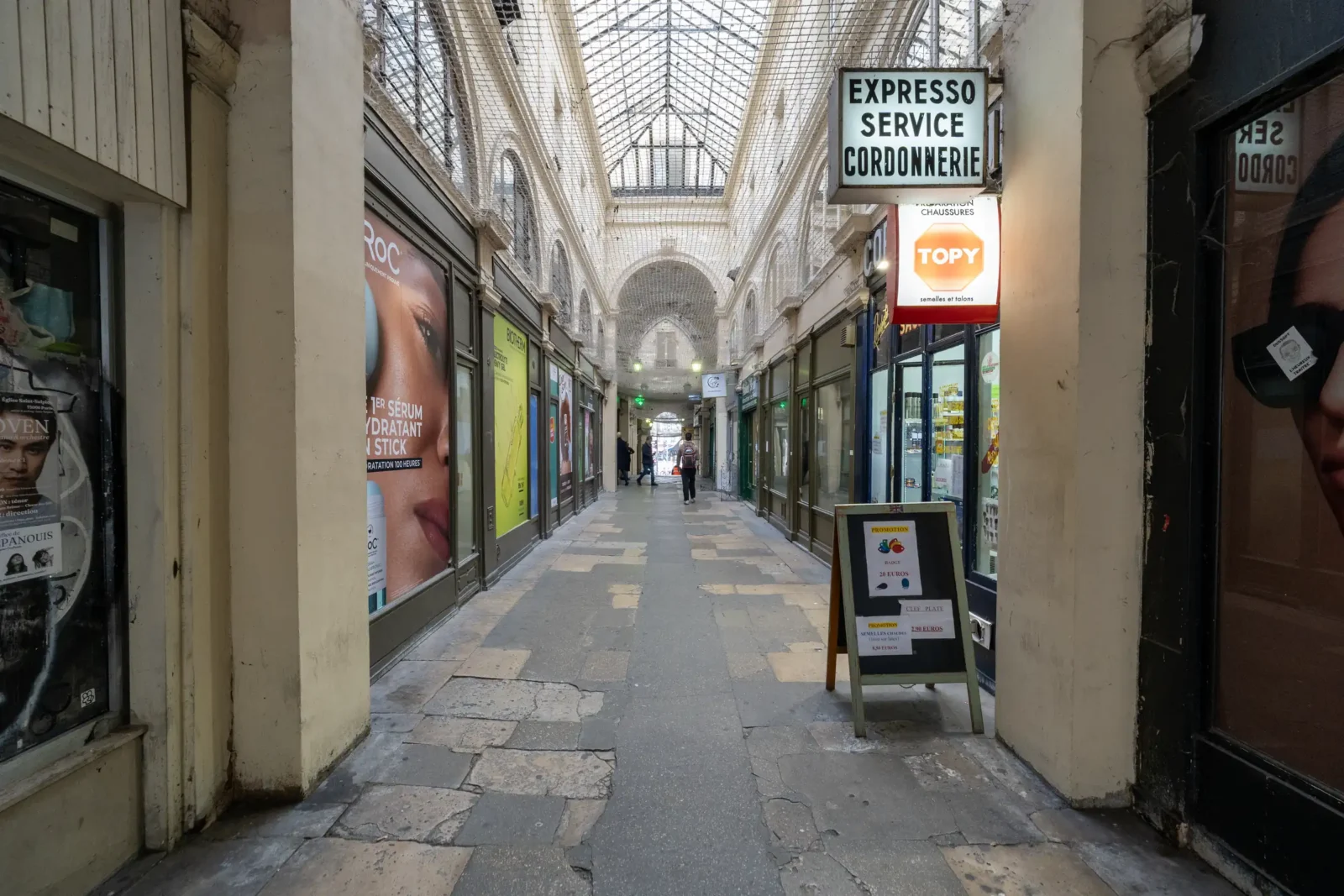 Le Passage Vendôme à Paris présente une allée couverte bordée de boutiques et publicités.