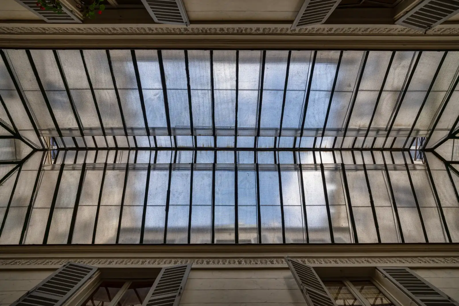 Vue en contre-plongée de la verrière grillagée du Passage Véro-Dodat à Paris sous ciel bleu.