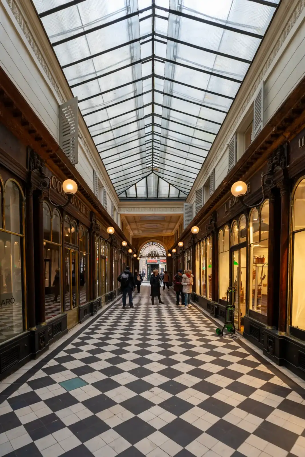 Des personnes marchent dans le Passage Véro-Dodat à Paris sous une verrière lumineuse.