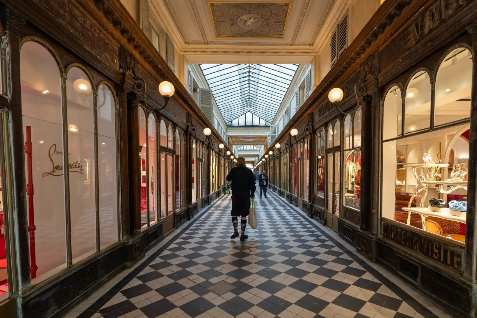 Un homme marche dans le Passage Véro-Dodat sous une verrière au sol damé.