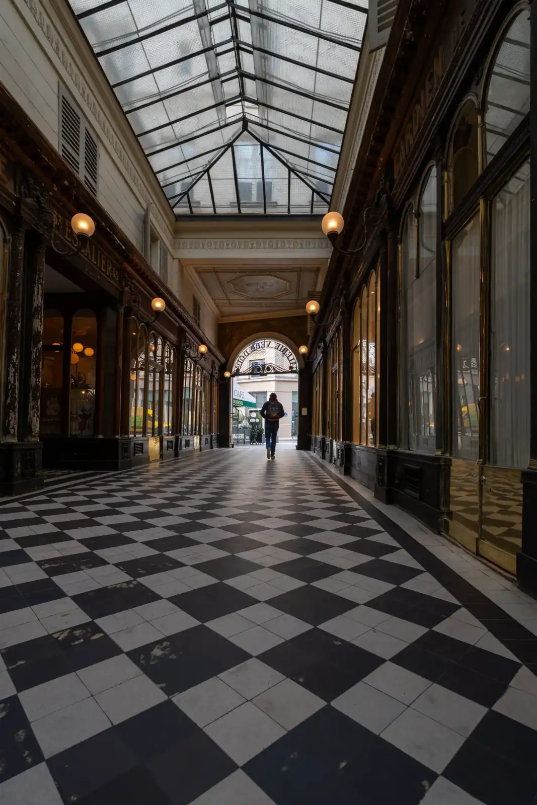 Une personne marche dans le passage couvert Véro-Dodat au sol en damier noir blanc.
