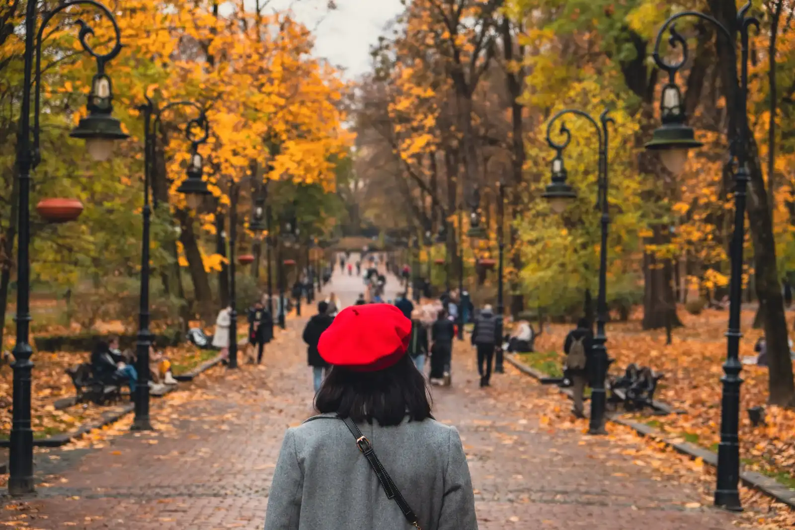 Une femme avec un béret rouge marche sur une allée automnale parisienne.