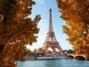 La tour Eiffel se dresse majestueusement derrière des arbres aux feuilles orangées.