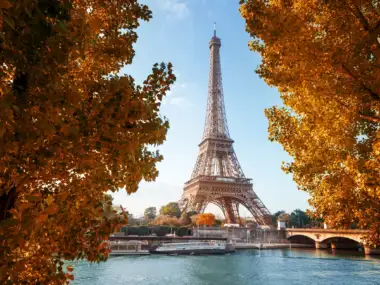 La tour Eiffel se dresse majestueusement derrière des arbres aux feuilles orangées.