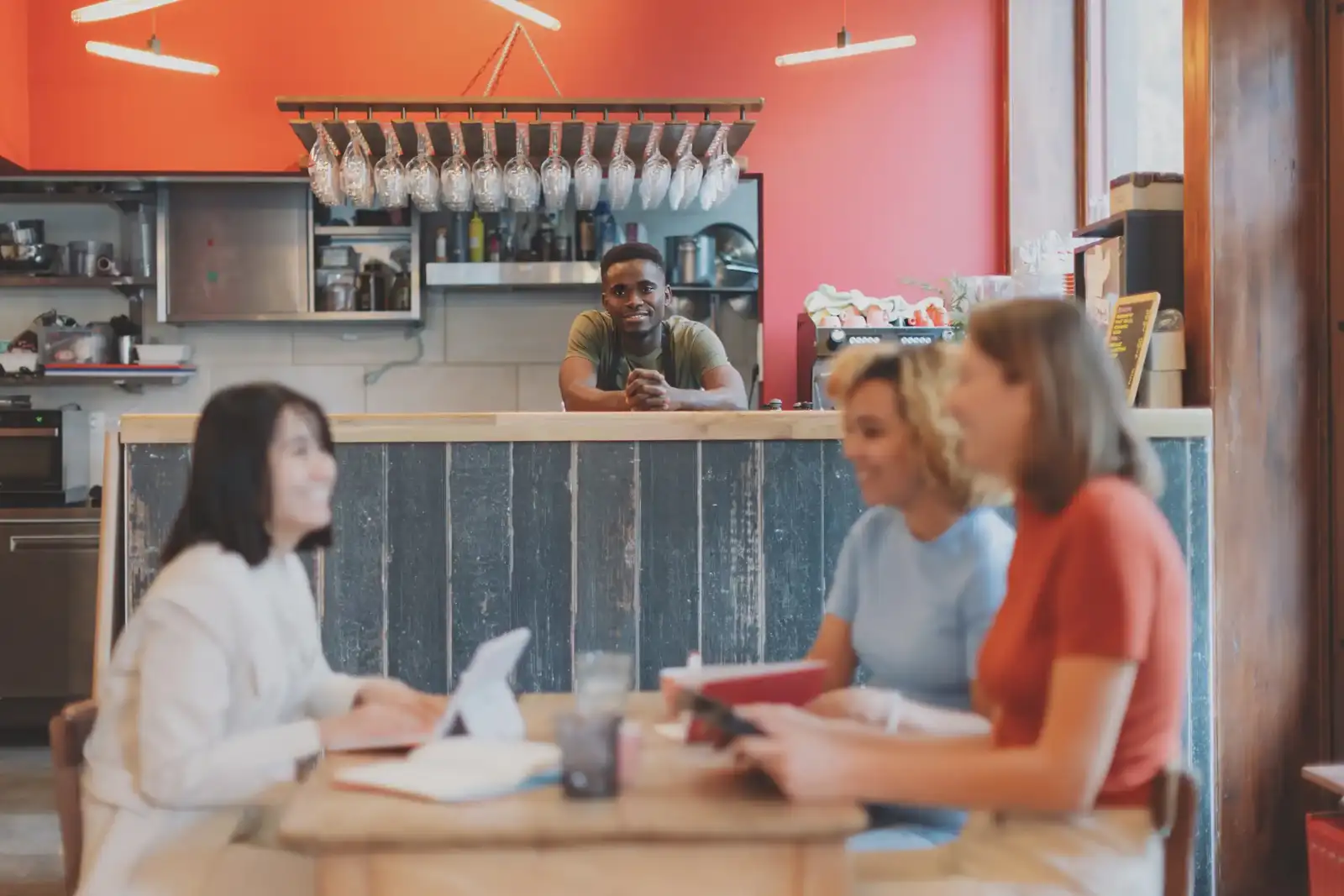 Trois femmes sourient autour d une table tandis qu un homme les observe du comptoir.