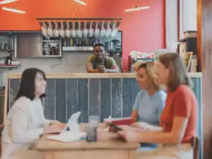 Trois femmes sourient autour d une table tandis qu un homme les observe du comptoir.