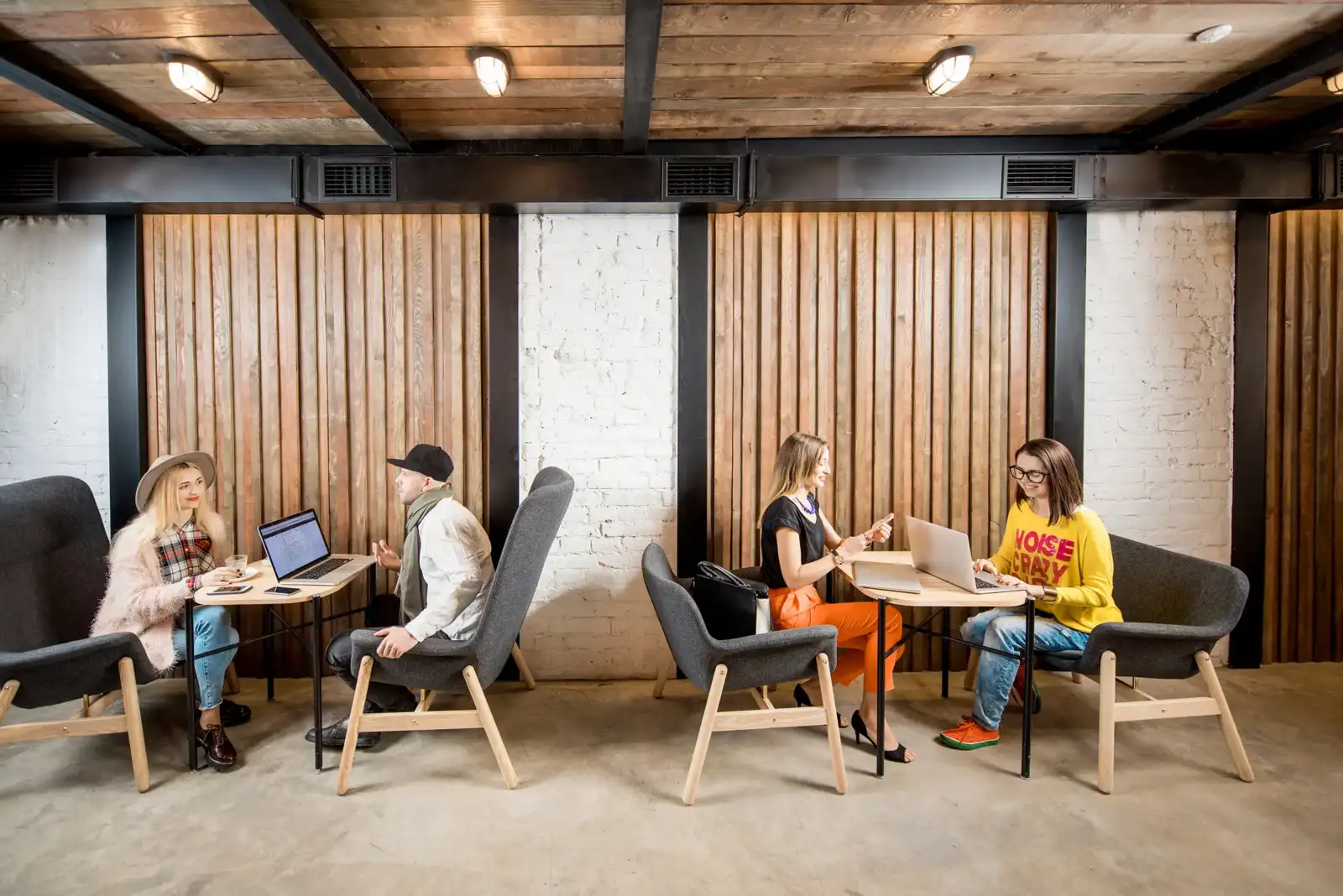 Quatre personnes travaillent ensemble avec des ordinateurs portables dans un espace de coworking élégant.