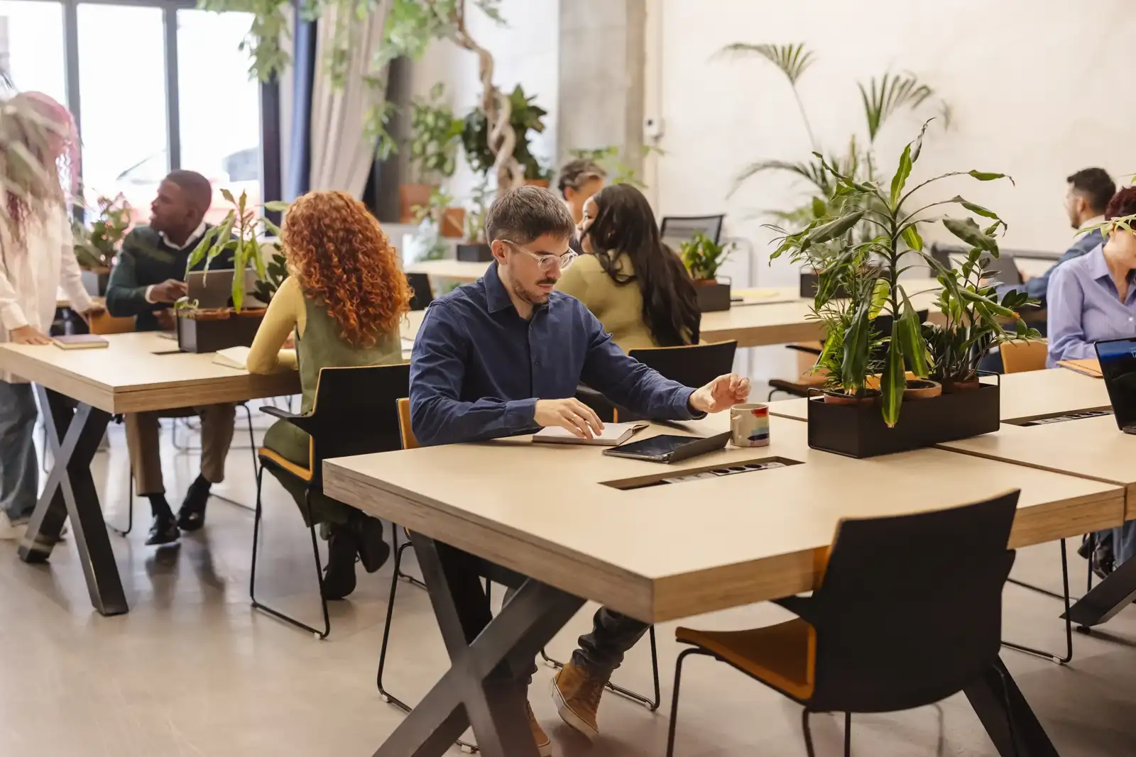 Des personnes travaillent ensemble autour de tables en bois dans un espace de coworking lumineux.