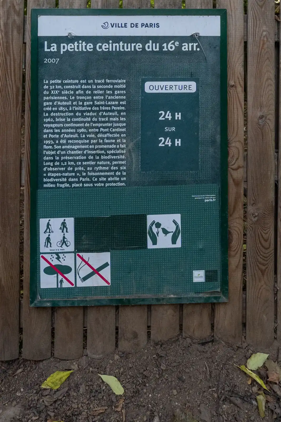 Un panneau d’information vert et blanc fixé sur une clôture en bois.