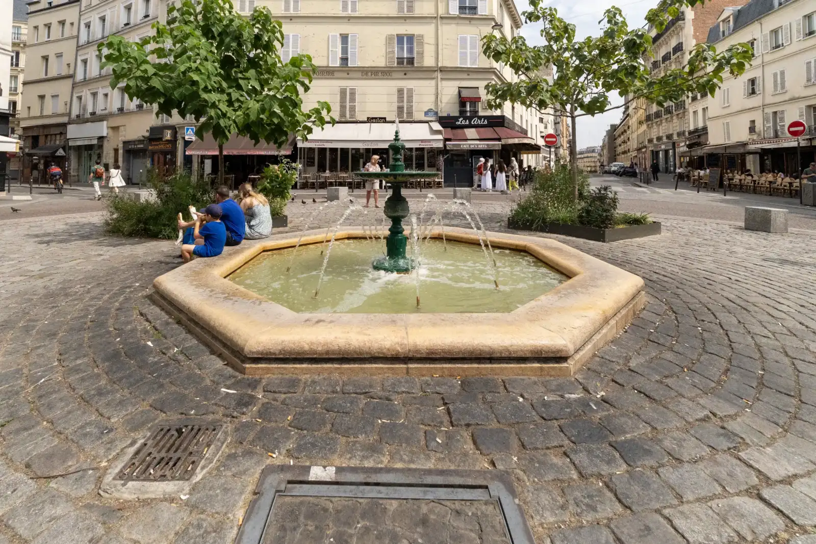 Une fontaine verte domine la place Contrescarpe pavée animée par des terrasses parisiennes.