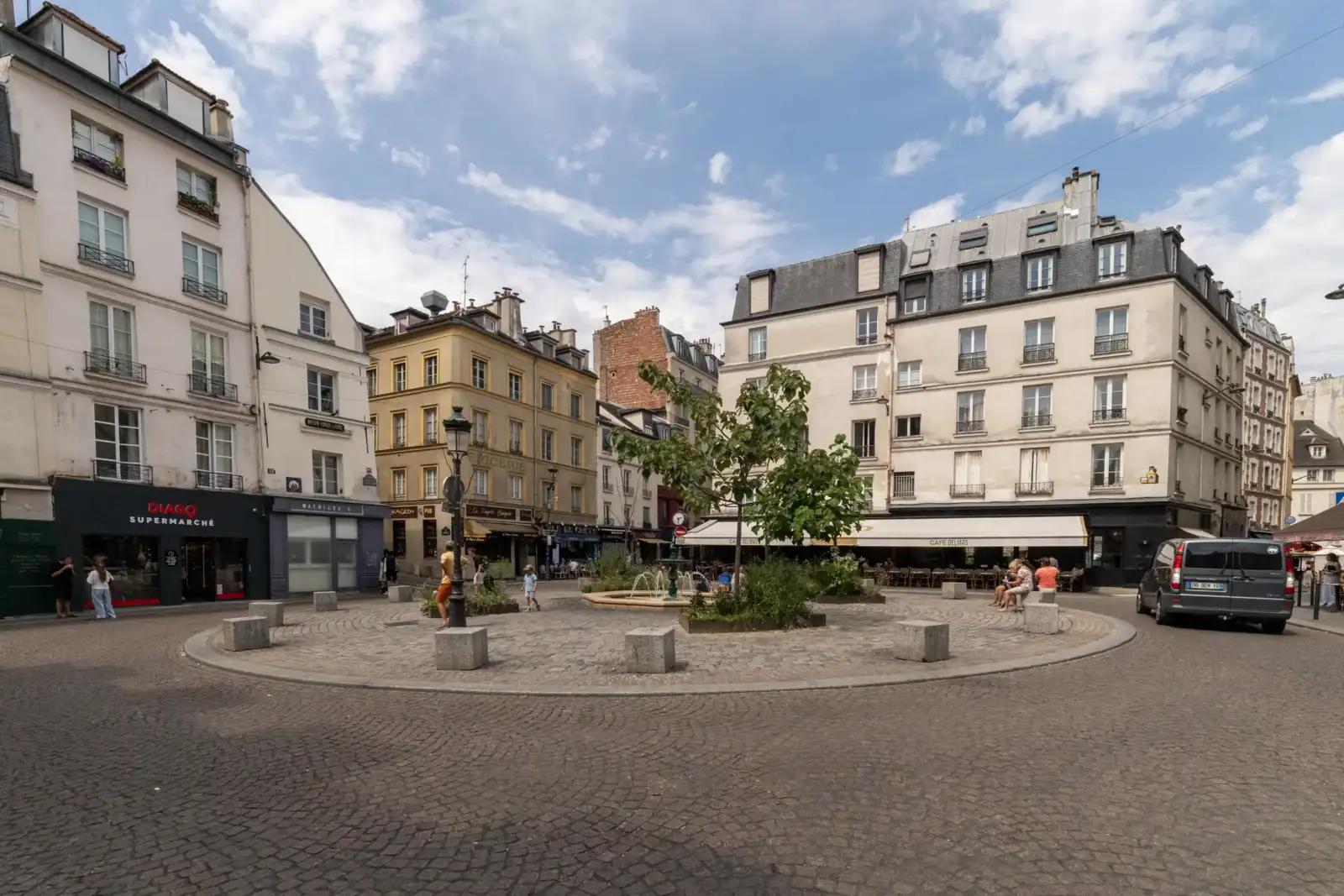 Une jolie place pavée parisienne bordée d'immeubles anciens sous un ciel nuageux.