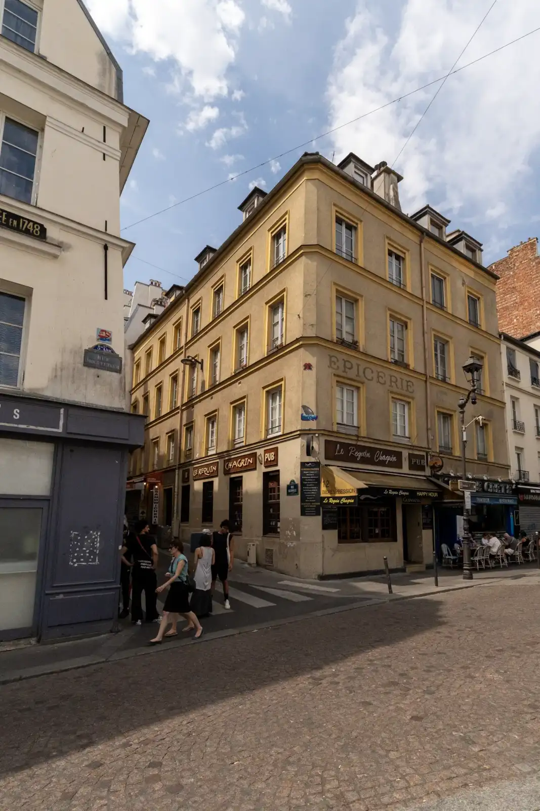 Vue de la façade d'un immeuble ancien beige situé sur une place parisienne animée.