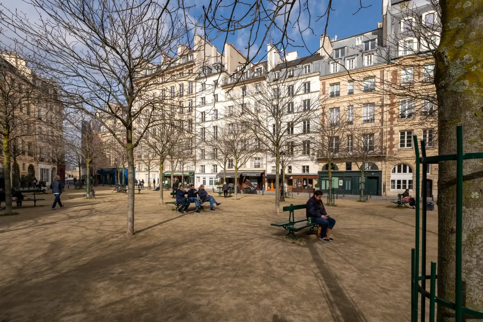 Des personnes se reposent sur des bancs dans la paisible Place Dauphine Ă Paris.