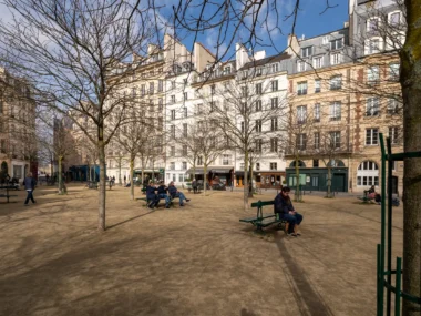 Des personnes se reposent sur des bancs dans la paisible Place Dauphine à Paris.