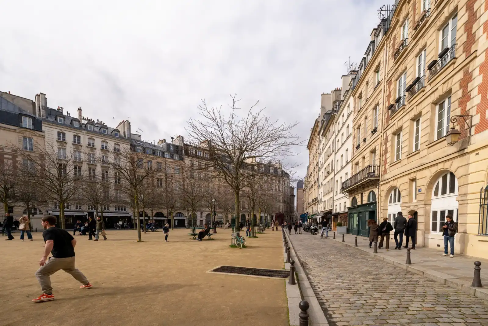 Des gens se promènent sur la place Dauphine entourée d'immeubles parisiens classiques en pierre.