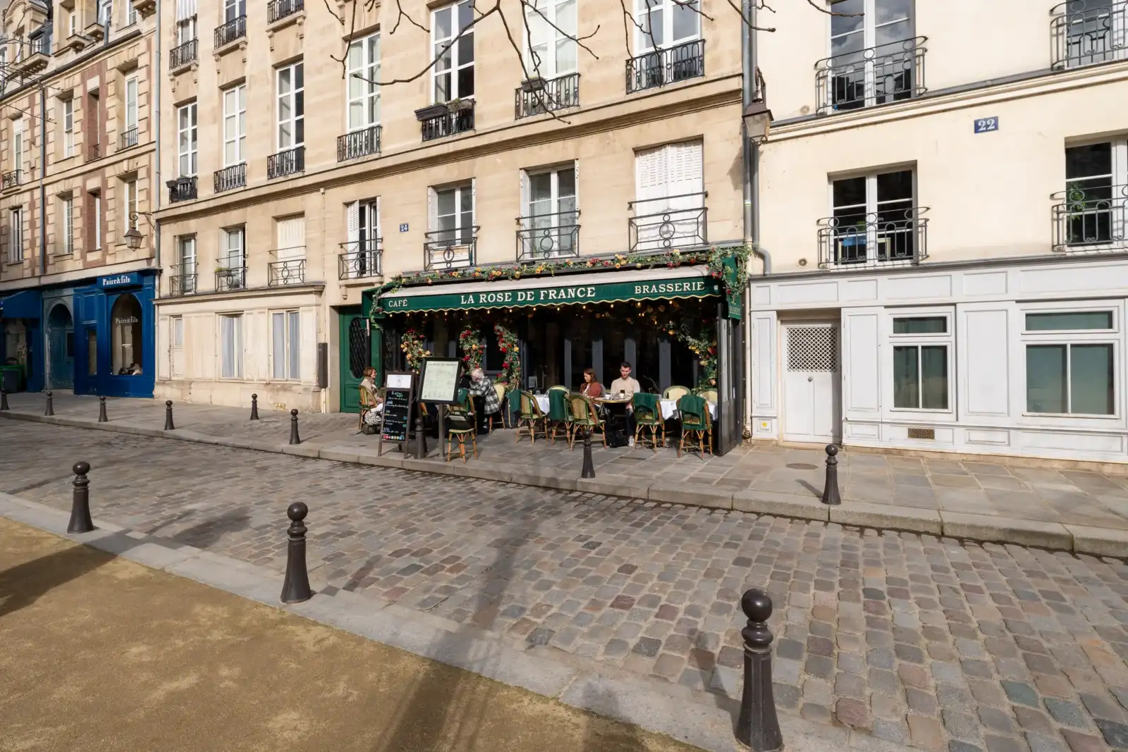 Des clients sont attablés à la terrasse fleurie du café La Rose de France.