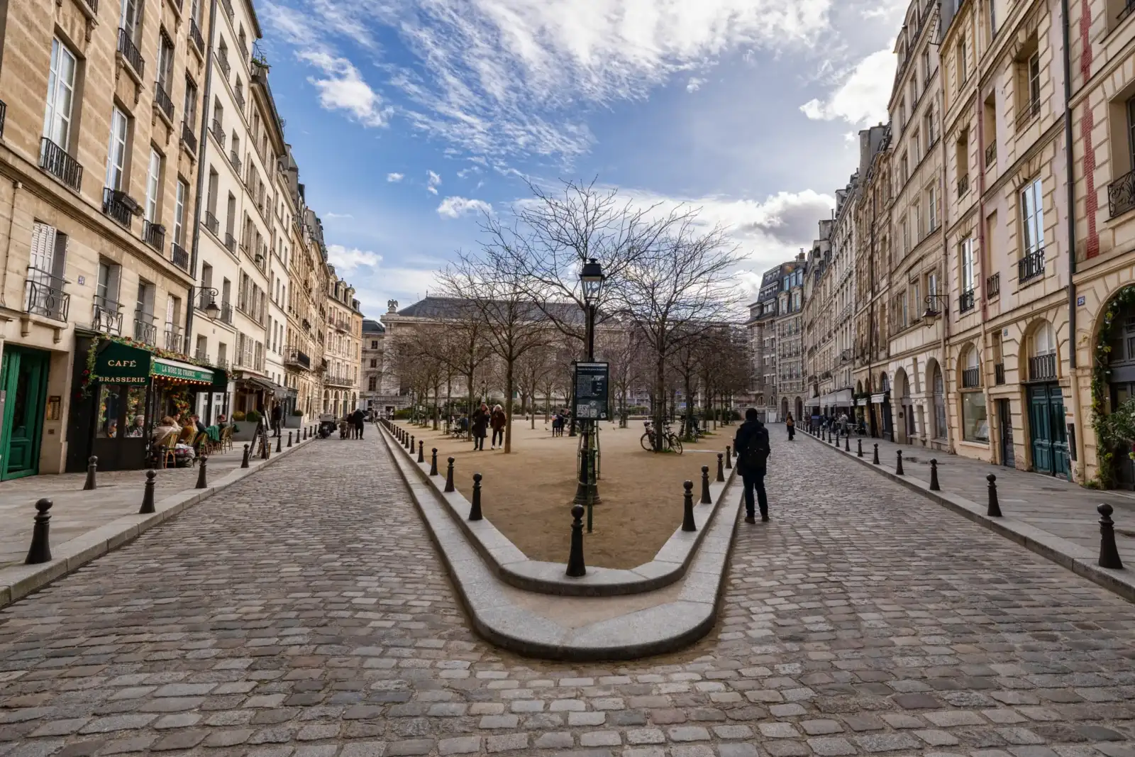 Vue en perspective de la Place Dauphine à Paris avec ses pavés et arbres.