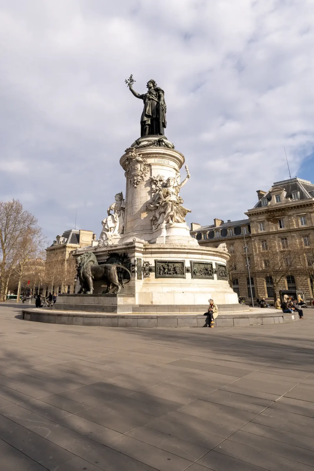La statue monumentale de la République trône sur une place pavée sous un ciel nuageux.