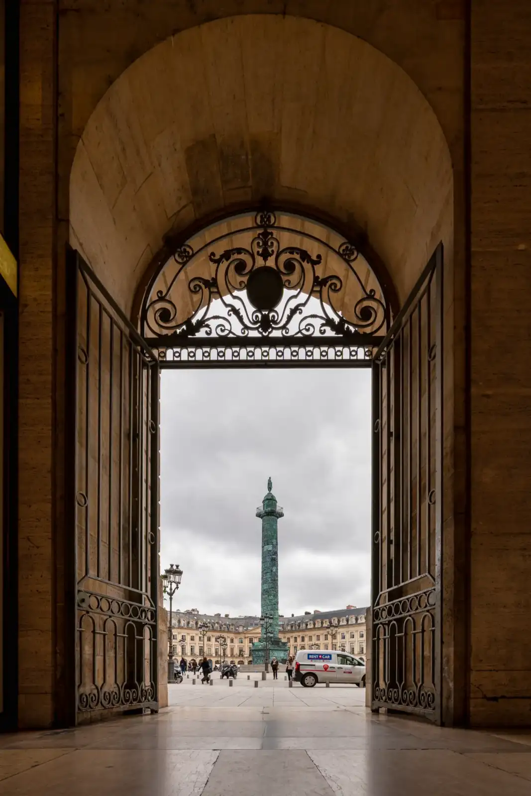 Vue encadrée par une porte monumentale sur la colonne Vendôme à Paris sous ciel gris.