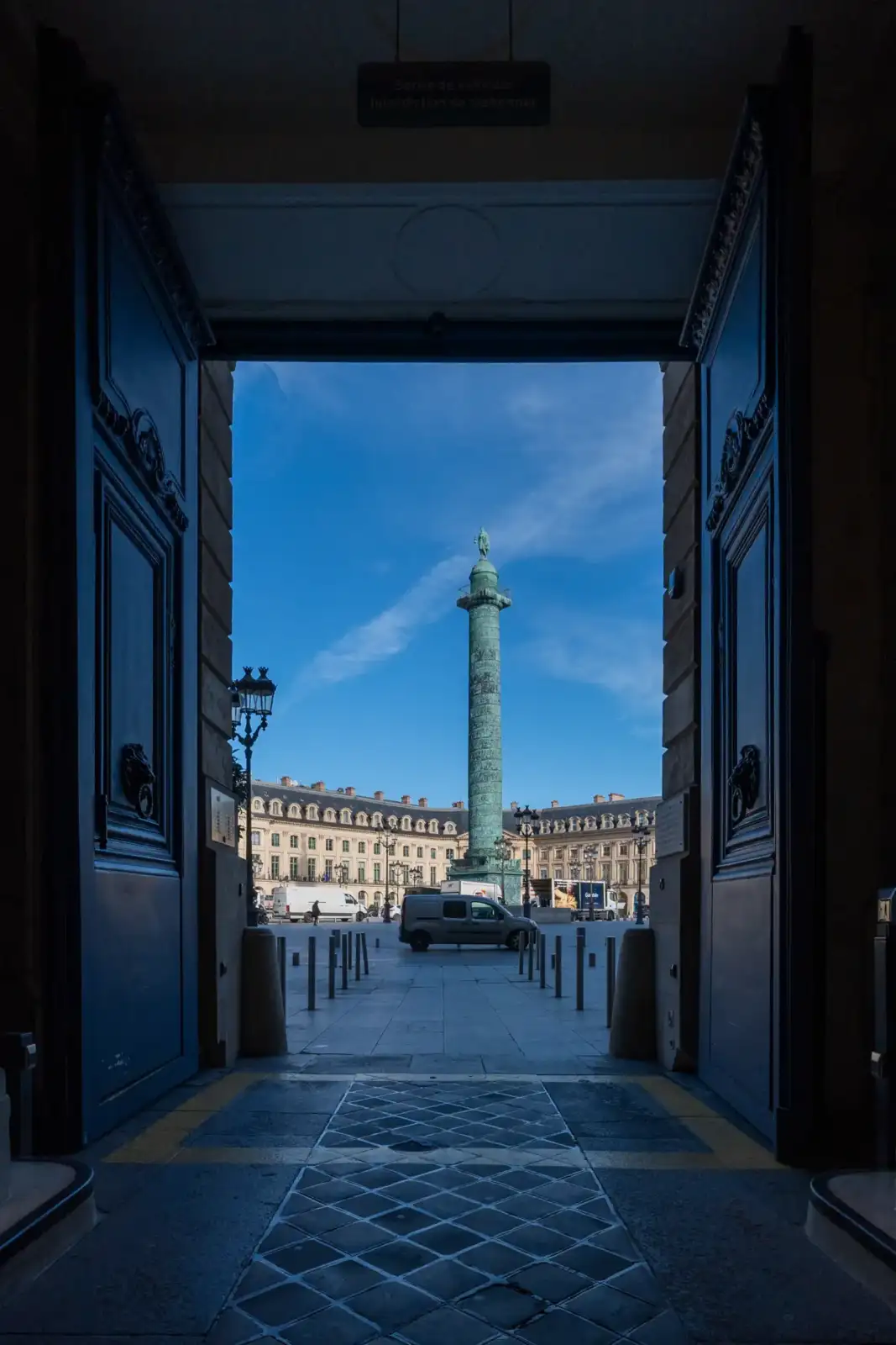 Vue encadrée de la colonne Vendôme depuis l'entrée sombre d'un immeuble parisien historique.