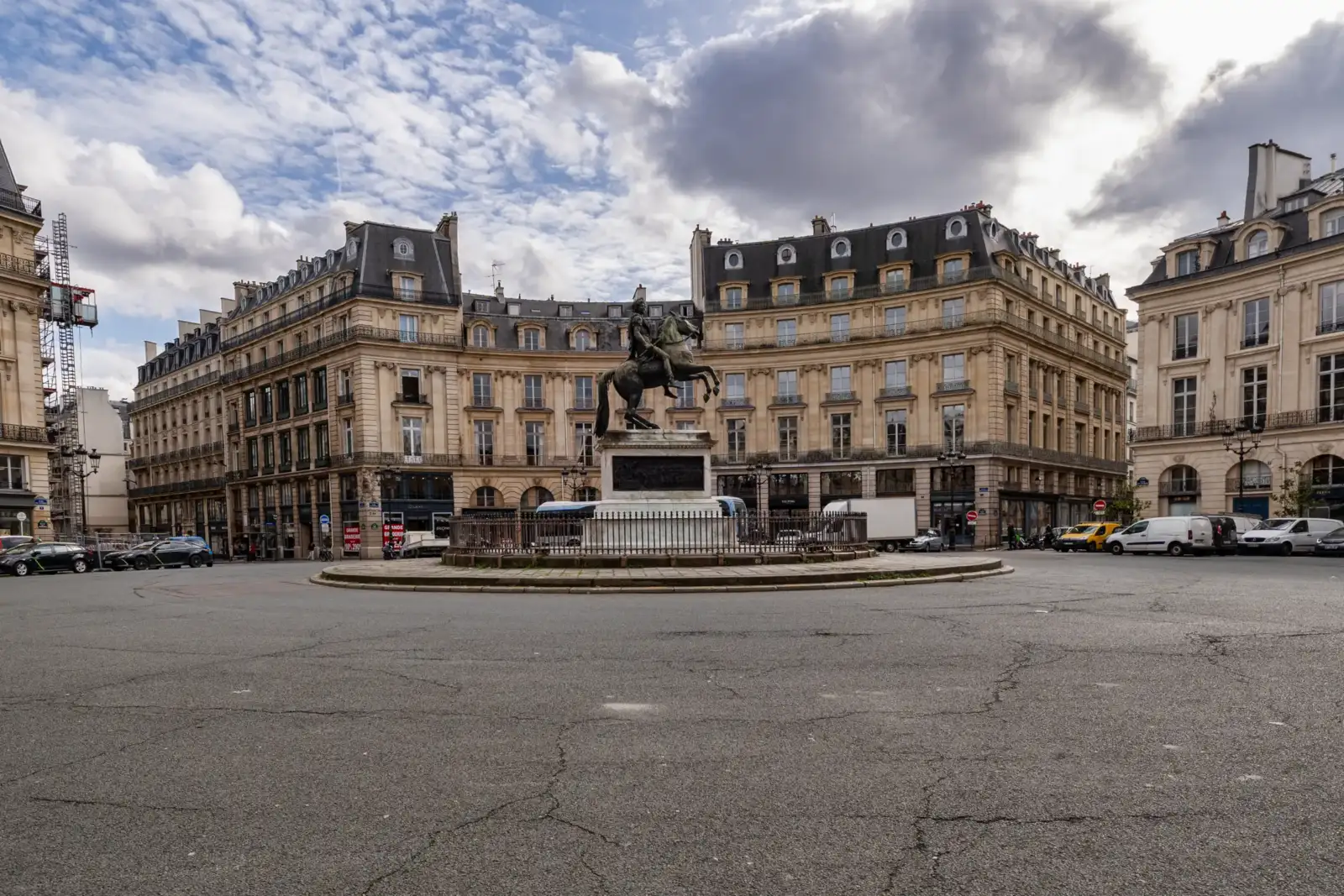 Statue équestre au centre de la place des Victoires entourée d'immeubles parisiens classiques.