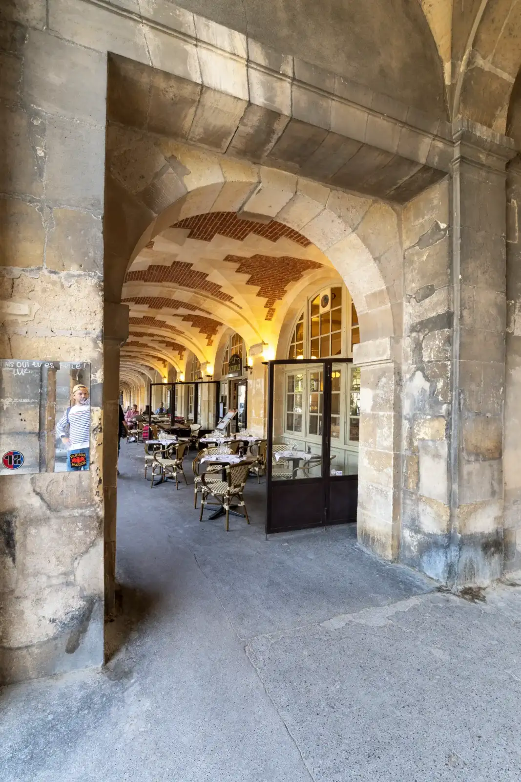 Une arcade en pierre dévoile les tables et chaises extérieures du restaurant de la Place des Vosges.