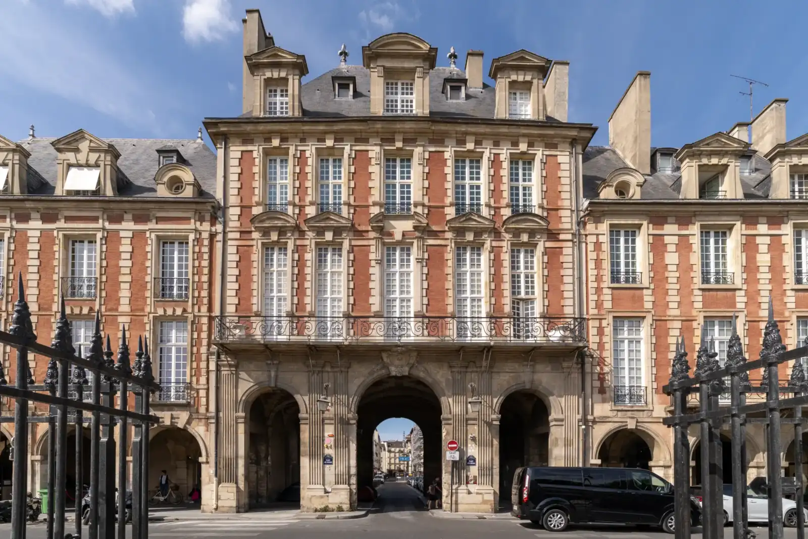 Façade classique en brique rouge et pierre avec des arcades sur une place parisienne.