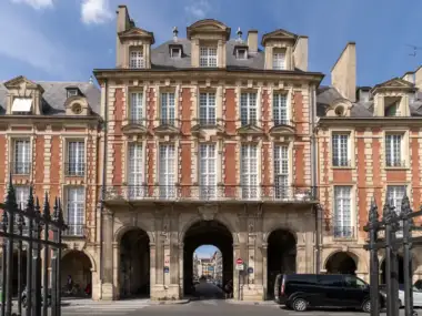 Façade classique en brique rouge et pierre avec des arcades sur une place parisienne.