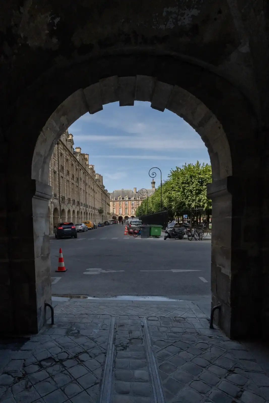Vue encadrée d'une rue parisienne bordée de bâtiments historiques sous un ciel bleu.
