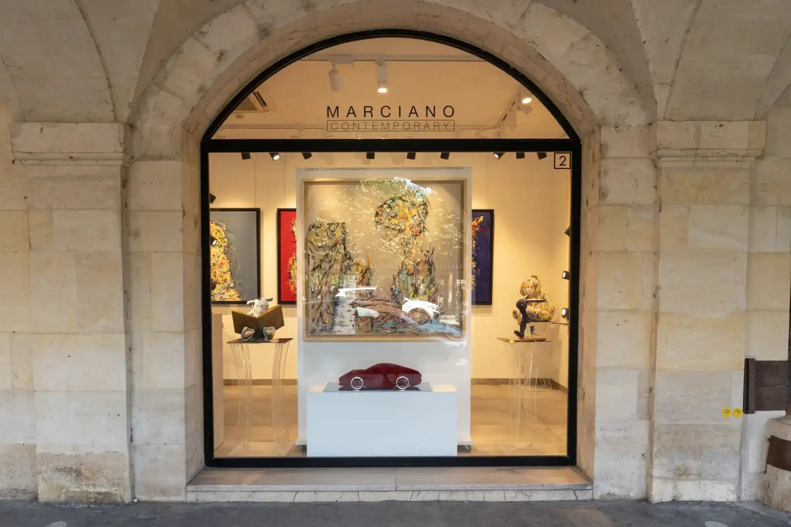 Sous les arcades de la Place des Vosges, une galerie d'art moderne expose des tableaux abstraits.