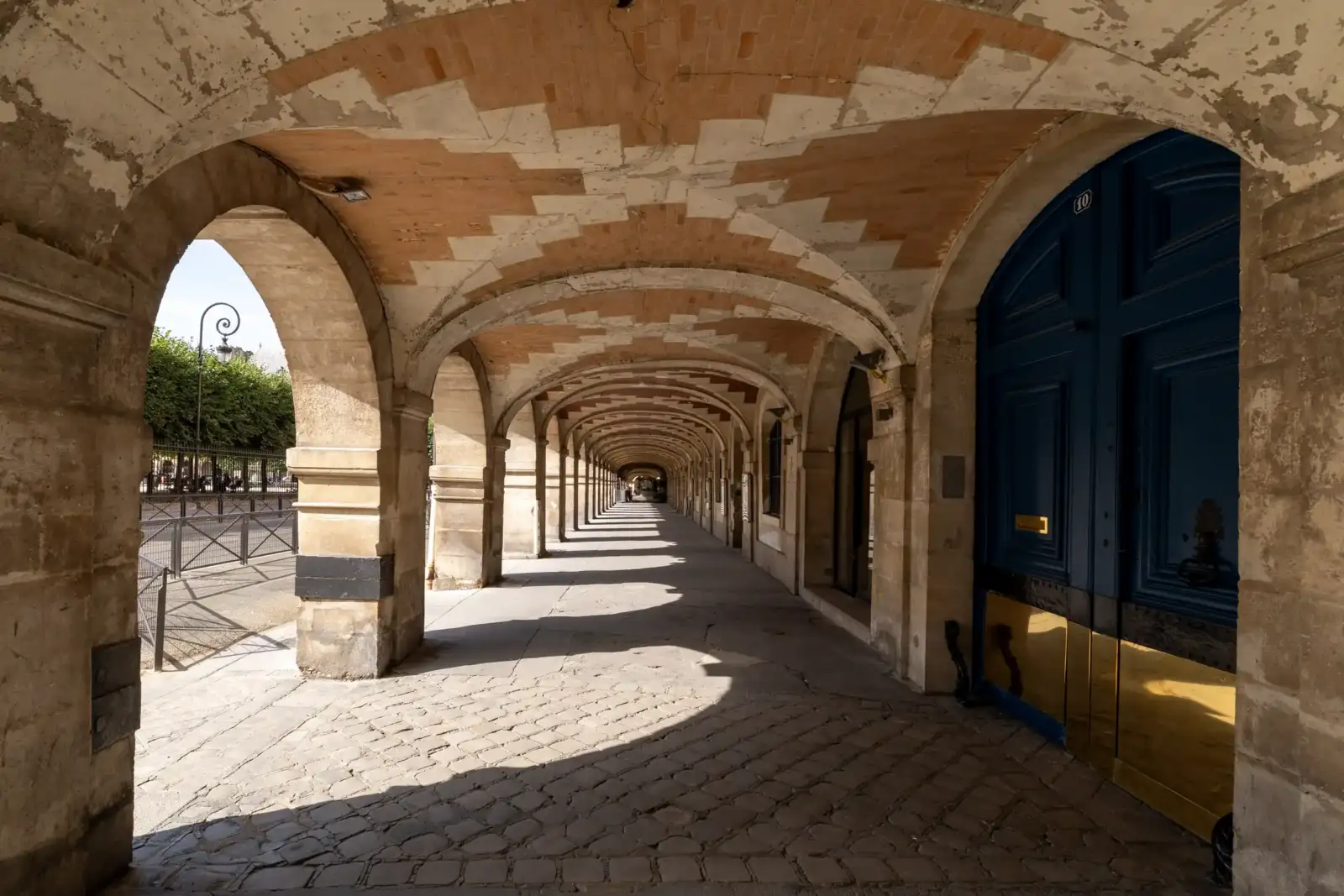 Vue en perspective des arcades voûtées en briques rouges de la place des Vosges.