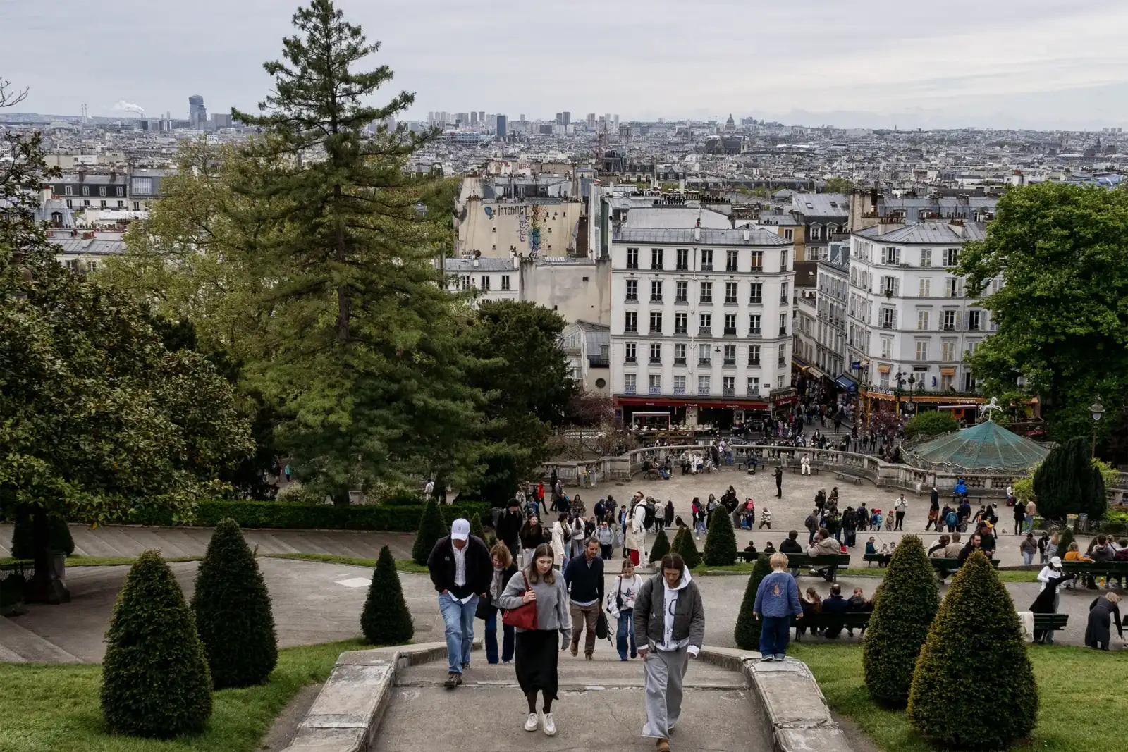 Des gens descendent les escaliers du parc de Montmartre avec Paris en arrière-plan.