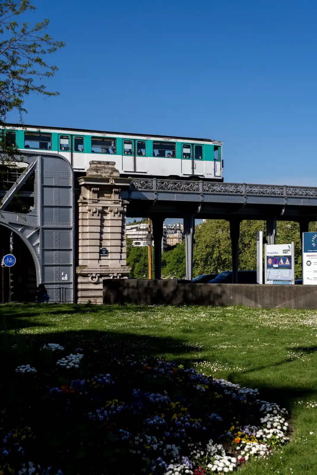 Une rame de métro parisien traverse le pont de Bir Hakeim sous un ciel bleu.