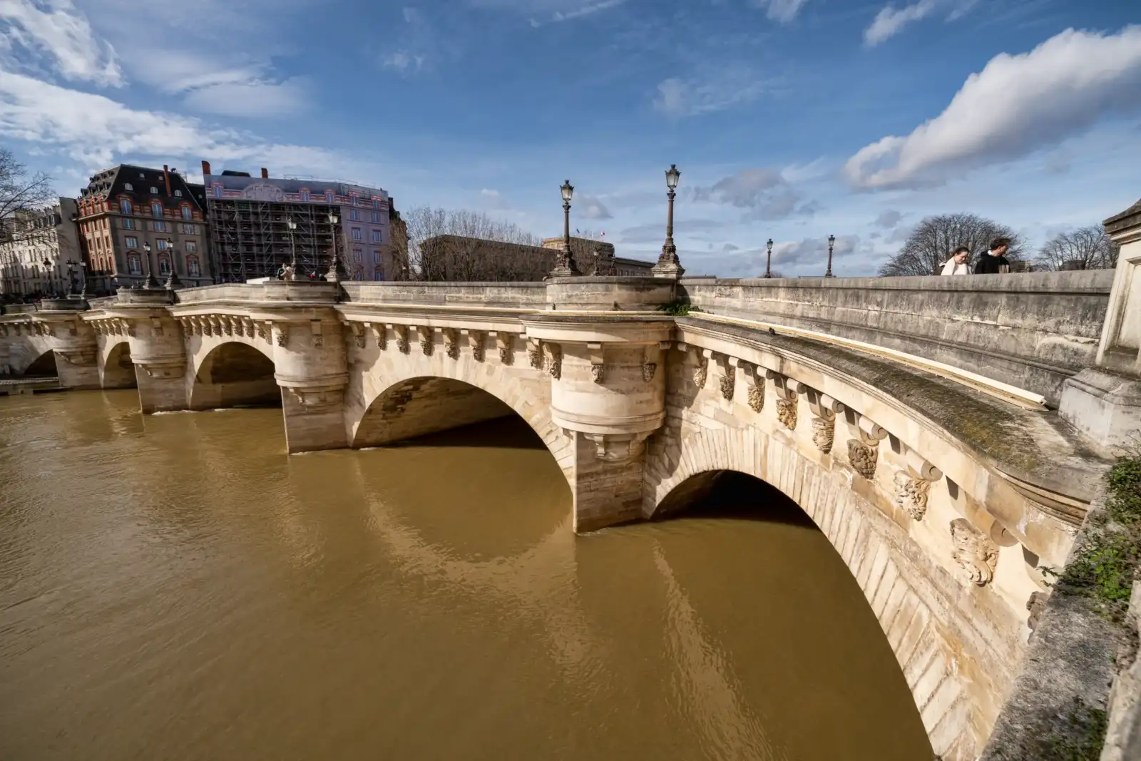 Le Pont Neuf en pierre enjambe la Seine sous un ciel partiellement nuageux à Paris.