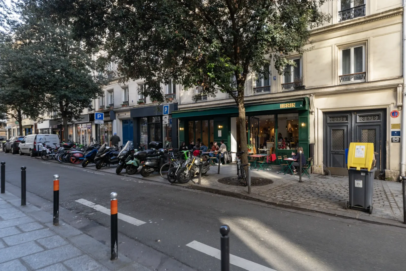 Façade d'un café parisien du quartier Sentier avec des clients en terrasse ensoleillée.