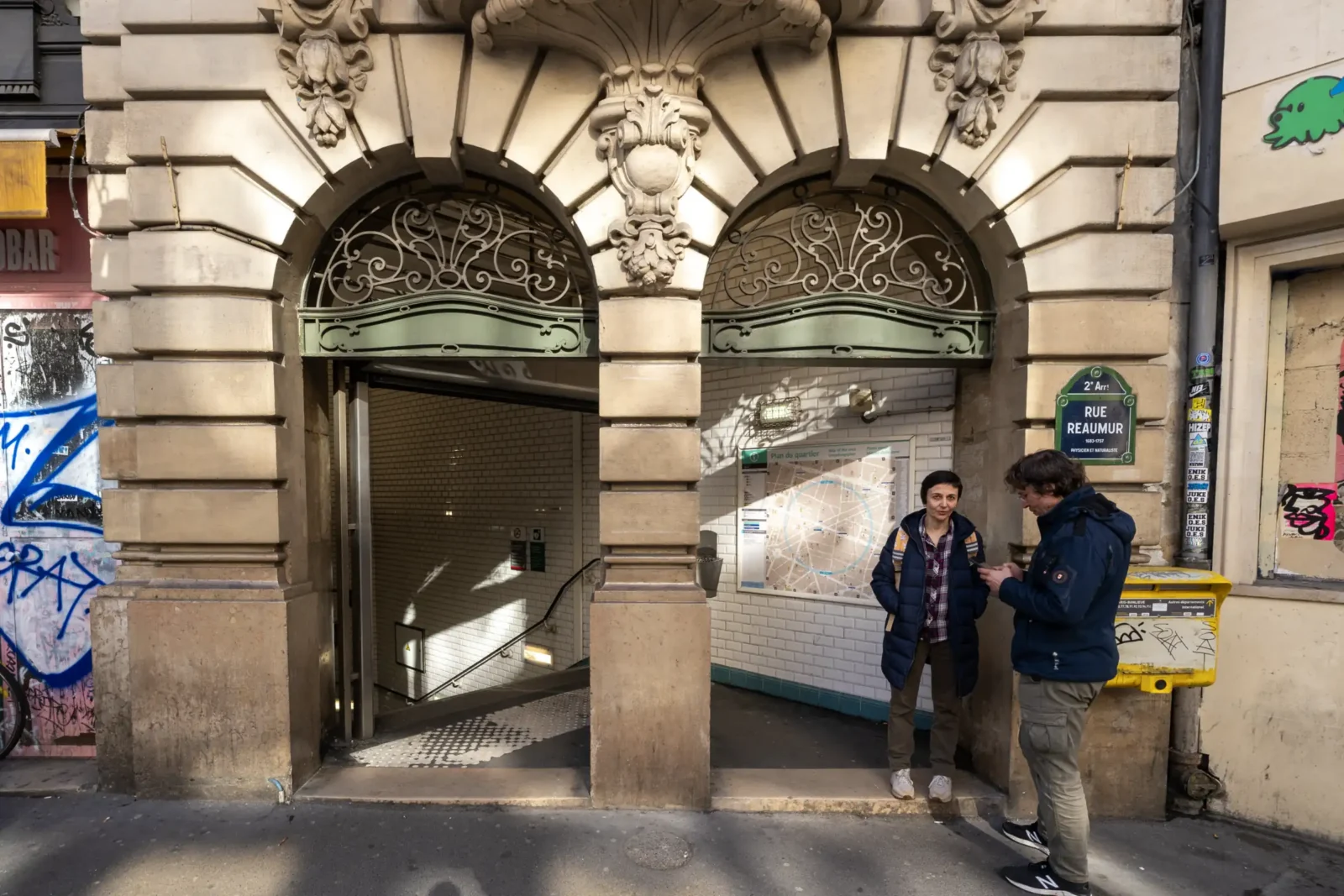 Deux personnes discutent devant l'entrée historique d'une station de métro rue Réaumur à Paris.