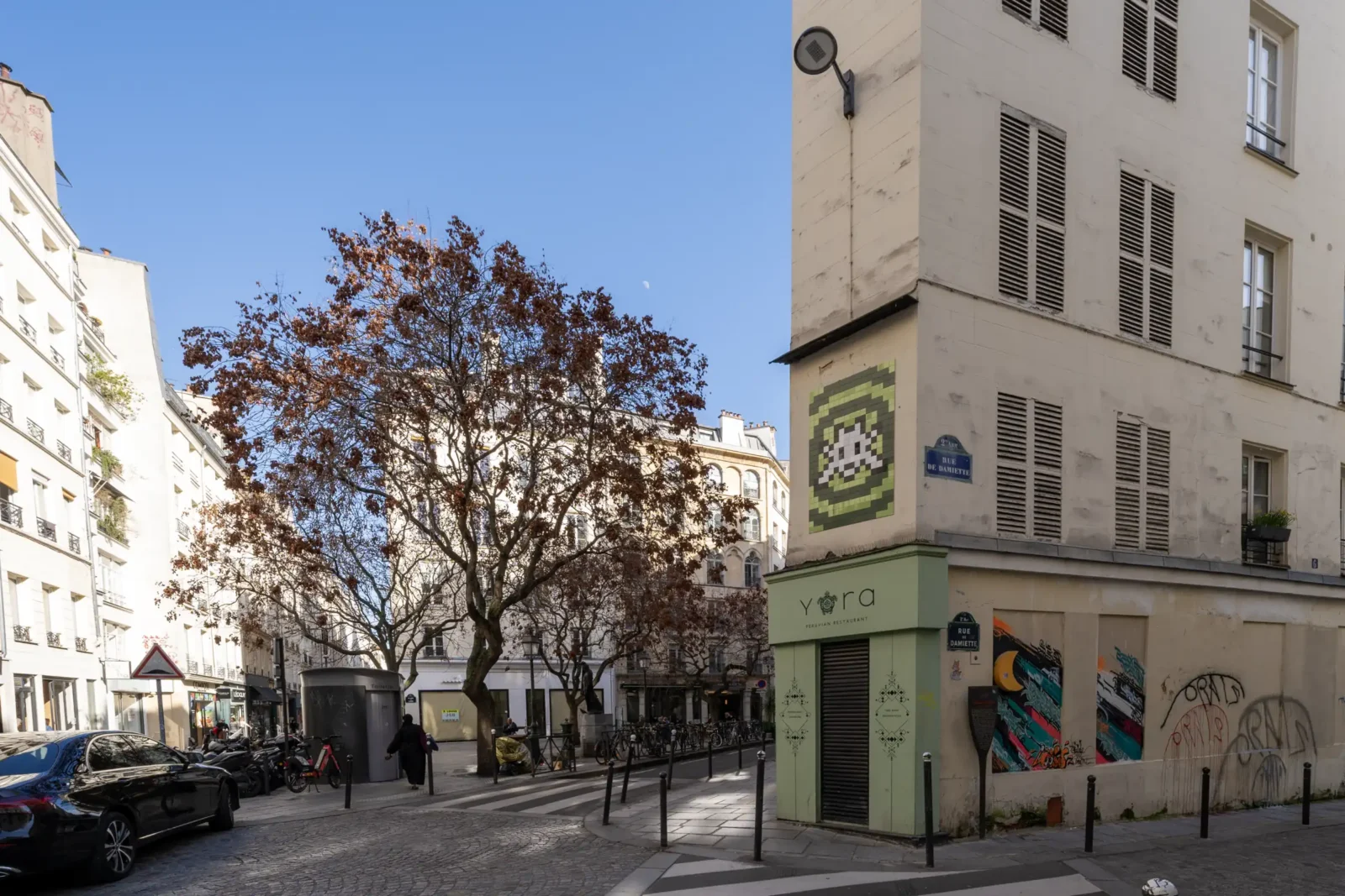 Une rue ensoleillée du quartier Sentier à Paris avec un immeuble d'angle et arbres.