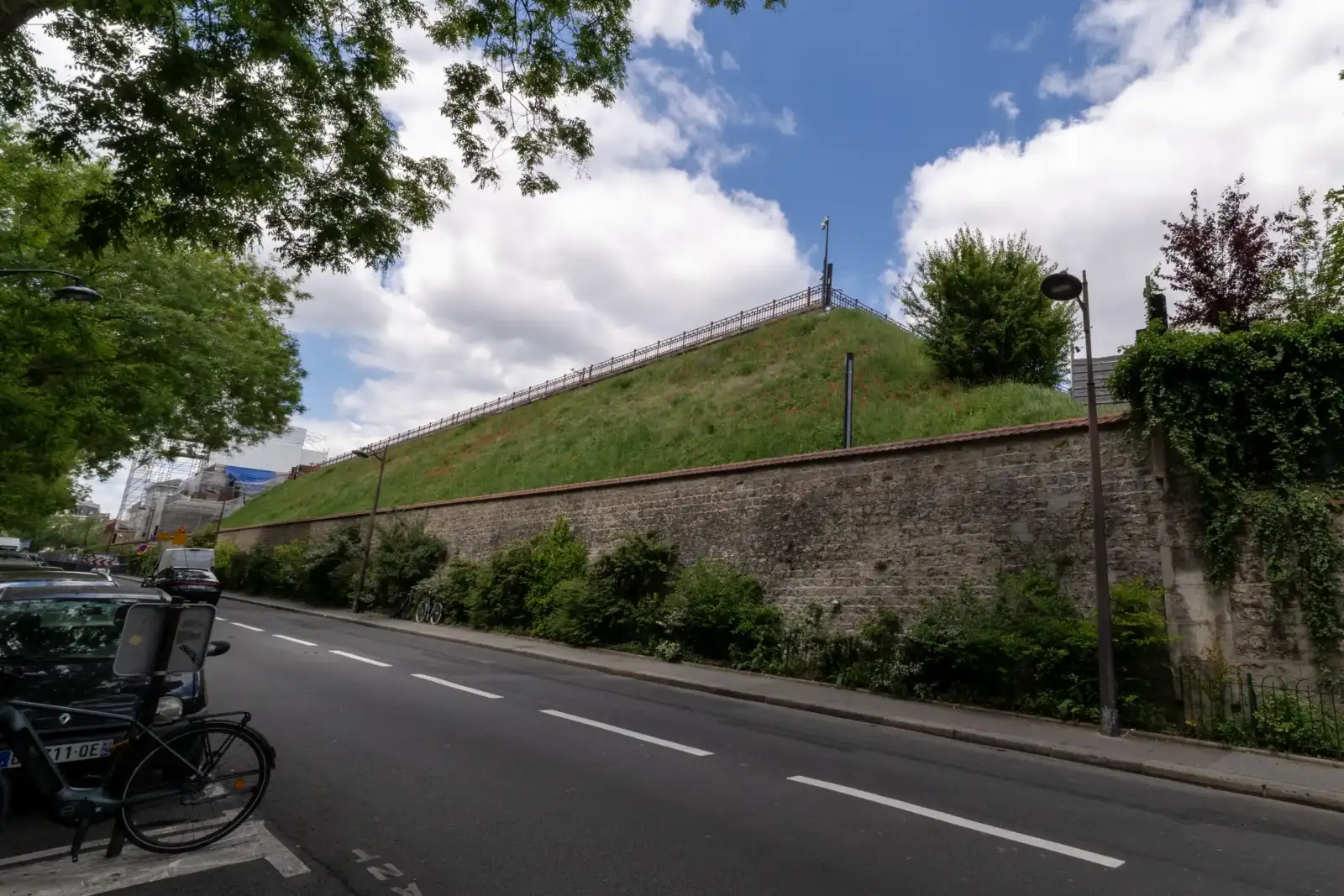 Une rue longe le mur en pierre du réservoir de Montsouris à Paris.
