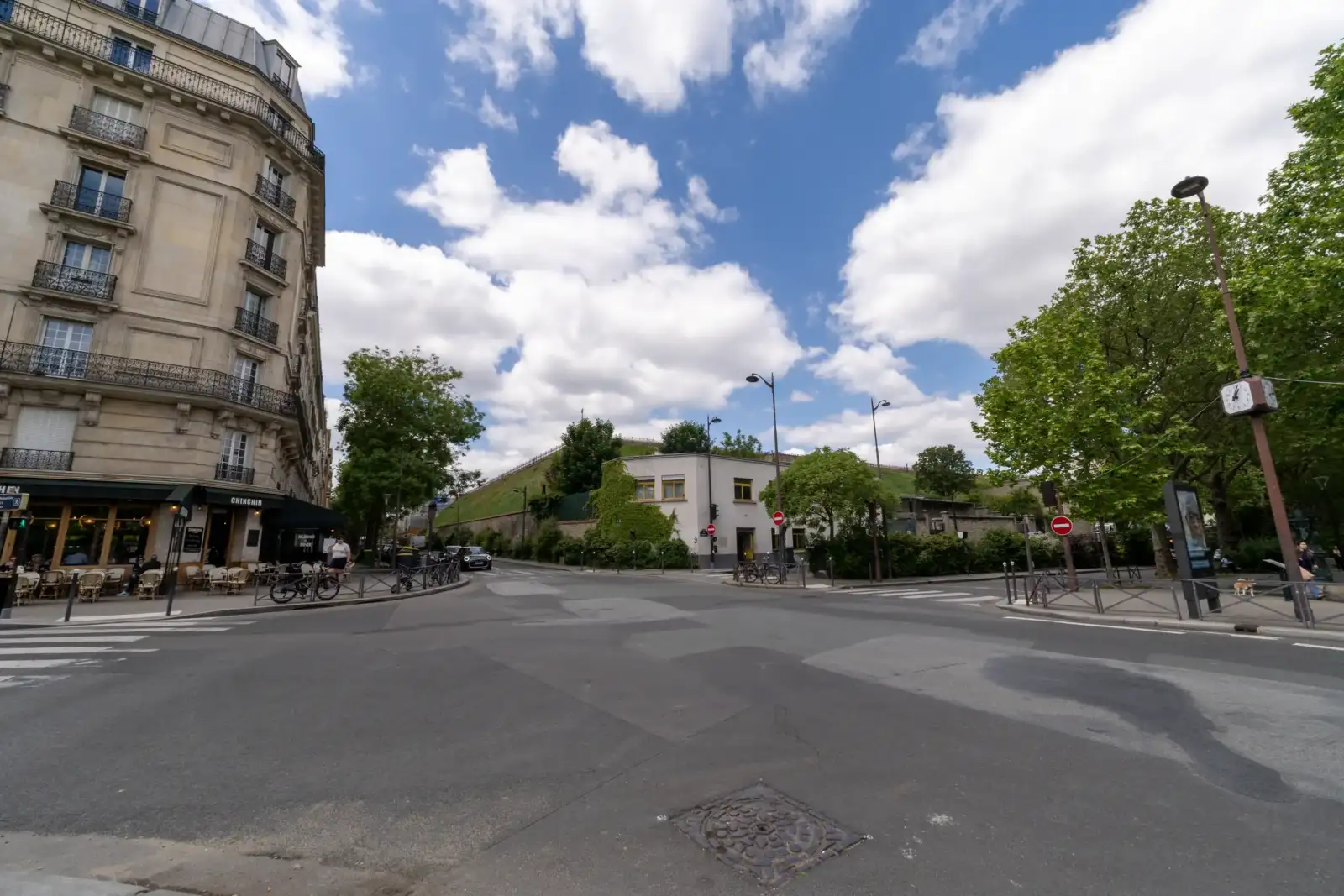 Une intersection parisienne bordée d'un grand immeuble et de verdure sous un beau ciel.