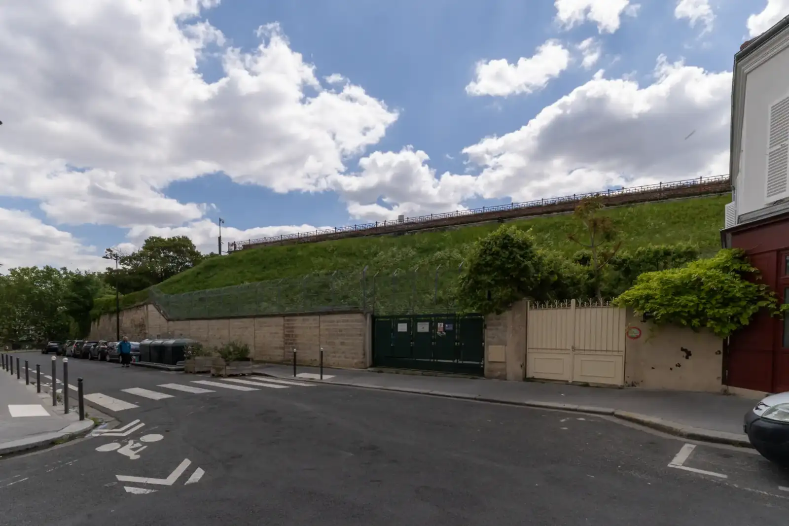Une rue urbaine longe le mur d'enceinte verdoyant du réservoir de Montsouris à Paris.