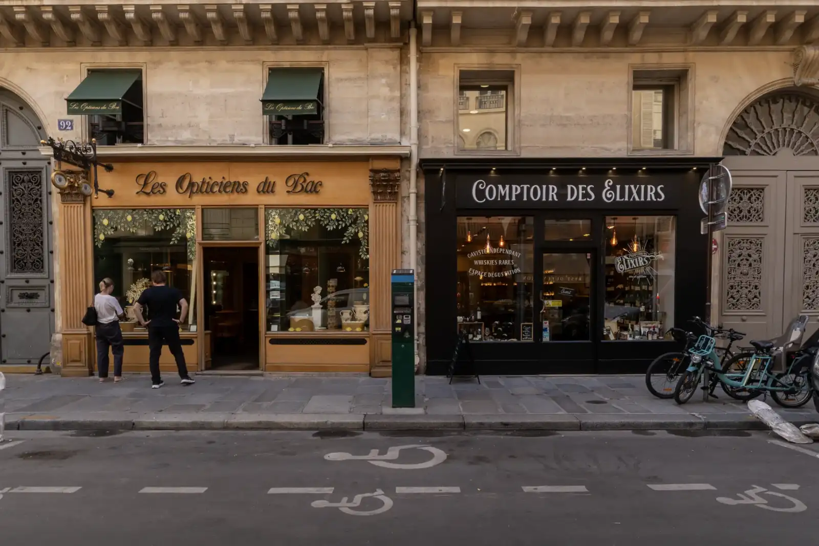 Deux personnes regardent la vitrine d'une boutique parisienne avec des devantures élégantes.