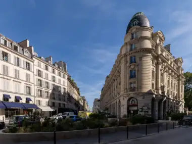Une perspective ensoleillée de la rue du Bac avec des bâtiments haussmanniens sous un ciel bleu.