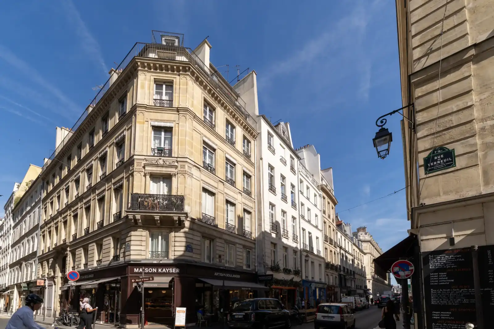 Une belle rue parisienne bordée d'immeubles haussmanniens sous un ciel bleu éclatant.
