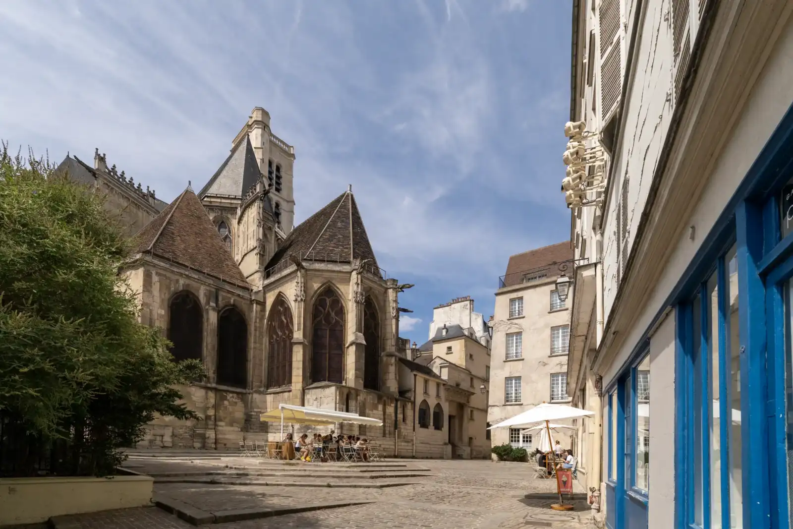 Une ruelle pavée de Paris dévoile la superbe façade de l'église Saint-Gervais sous un beau ciel bleu.