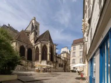 Une ruelle pavée de Paris dévoile la superbe façade de l'église Saint-Gervais sous un beau ciel bleu.