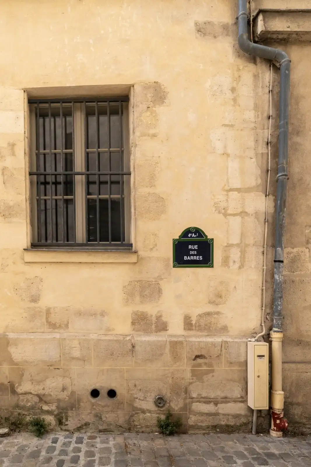 Une plaque de rue parisienne indiquant la rue des Barres sur un mur beige.